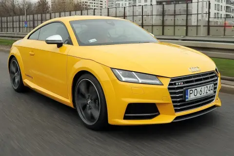 Żółte Audi TT RS, jedna z nowszych audi tt generacji, pędzi po drodze.