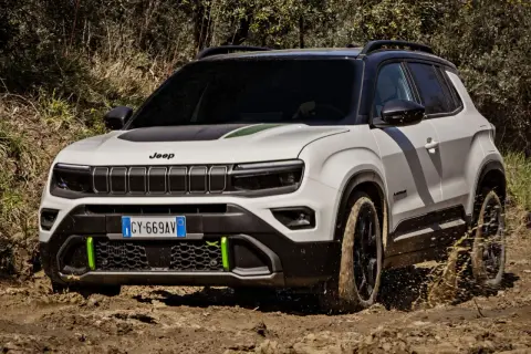 Biały terenowy SUV Jeep z zielonymi akcentami pokonuje błotniste wyzwanie, chlapiąc wodą.