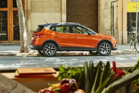 Pomarańczowy suv, crossover, zaparkowany na ulicy w mieście, obok drzewa i budynku.