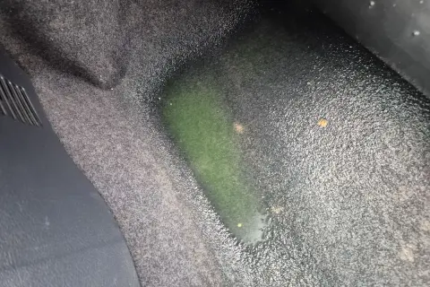 Zielona, mokra podłoga w samochodzie od strony kierowcy. Wygląda na wyciek płynu chłodniczego.