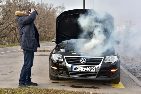Mężczyzna z przerażeniem patrzy na dym spod maski i czuje zapach spalenizny. Awaria Volkswagena na drodze.