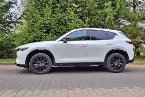 Biała Mazda CX-5 na tle zieleni. Zastanawiasz się nad jej spalaniem? Ten SUV oferuje świetny kompromis między osiągami a ekonomią.
