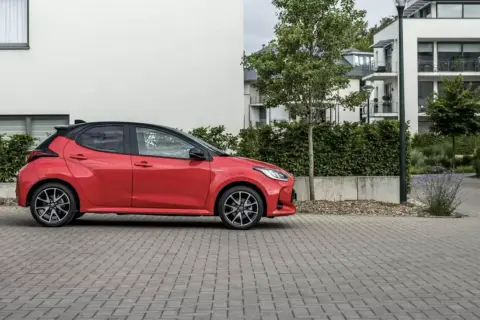 Czerwone, małe, niezawodne auto stoi na brukowanym podjeździe przed nowoczesnym budynkiem.