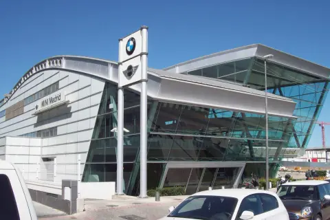 Nowoczesny salon MINI Madrid z logo BMW. W tle widać budynek i dźwig budowlany, a przed nim zaparkowane samochody, gotowe do akcje przywoławcze BMW.
