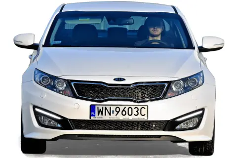 Białe auto z Korei Południowej, model Kia, z młodym kierowcą za kierownicą.