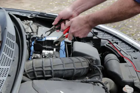 Ręce podłączają kable do akumulatora, by rozwiązać problem nagłego wzrostu spalania diesel.