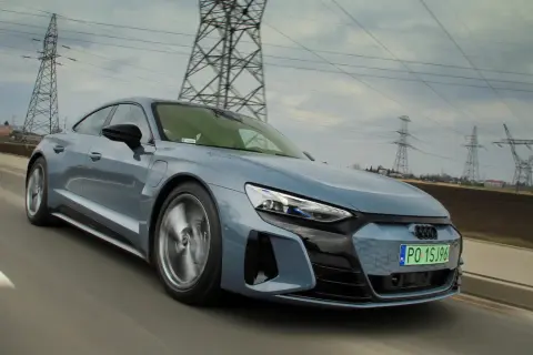 Szary, sportowy Audi GT jedzie po drodze, a w tle widać linie energetyczne i słupy.