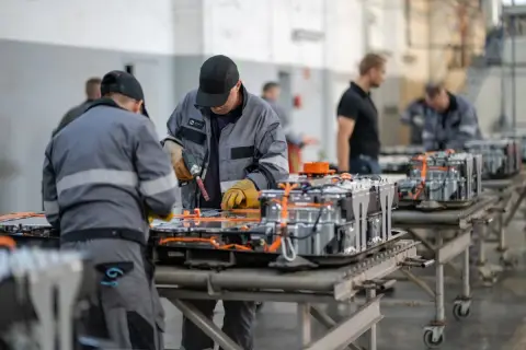Pracownicy montują moduły baterii do pojazdów elektrycznych. To przyszłość elektromobilności i praca dla wielu.
