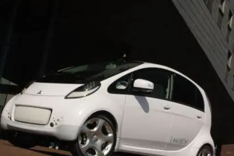 Biały, kompaktowy Mitsubishi i-MiEV stoi przed nowoczesnym budynkiem.
