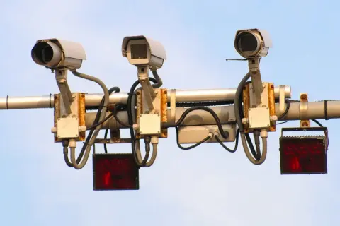 Trzy kamery monitorujące ruch drogowy, każda z migającym **system red light** pod nią.