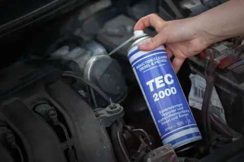 Ręka trzyma puszkę TEC 2000, wykonując czyszczenie kolektora dolotowego silnika.