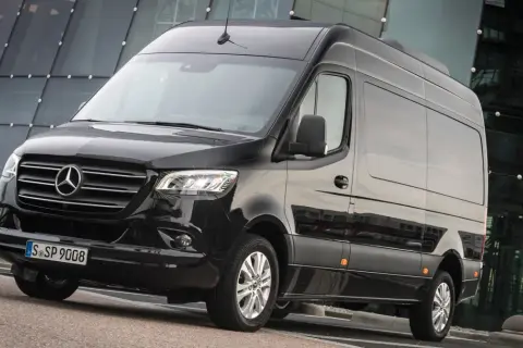 Czarny Mercedes-Benz Sprinter, jeden z najlepszych samochodów dostawczych, zaparkowany przed nowoczesnym budynkiem.