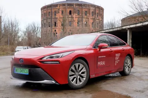 Czerwona Toyota Mirai z napisem "Zasięg na jednym tankowaniu do 650 km" stoi przed zabytkową gazownią.