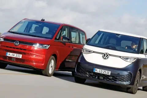 Dwa minivany Volkswagen: czerwony i dwukolorowy, jadące po drodze.