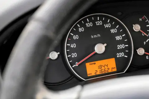 Zbliżenie na deskę rozdzielczą samochodu. Widoczny prędkościomierz, wskaźnik paliwa i temperatury. Cyfrowy wyświetlacz pokazuje przebieg 216621 km.