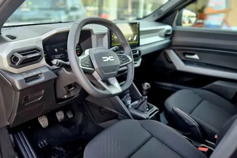 Wnętrze Dacia Bigster: kierownica z logo, ekran multimediów, dźwignia zmiany biegów i czarne siedzenia.