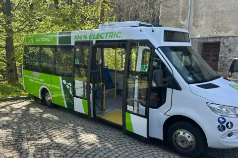 Nowy, zielono-biały bus elektryczny "Automety" z napisem "100% ELECTRIC" stoi na bruku.