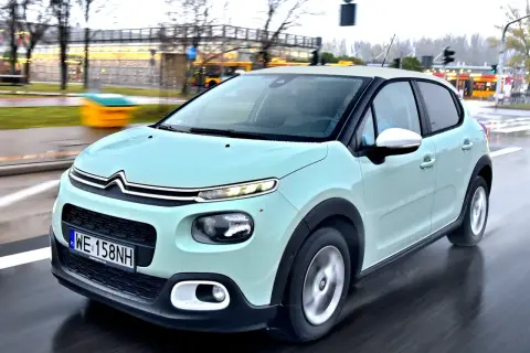 Jasnozielony Citroën C3, jeden z francuskich marek samochodów, jedzie po mokrej drodze.