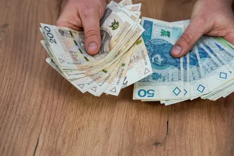 Dłonie trzymają stosy polskich banknotów 200 zł i 50 zł. Może to być zapłata za kartę pojazdu leasing.