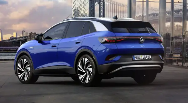 Niebieski VW ID.4 z imponującym zasięgiem, zaparkowany na tle miejskiego krajobrazu z mostem w tle.