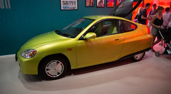 Jasnozielona Honda Insight, pierwsza hybryda na rynku, prezentowana na wystawie. To najlepsza hybryda, która wyznaczyła nowe standardy.