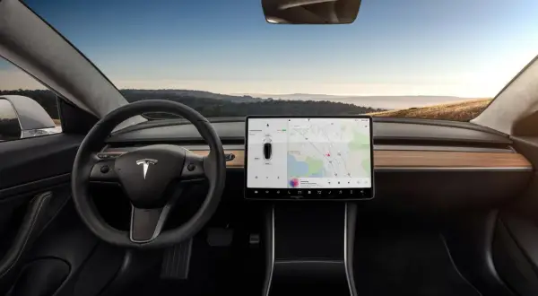 Wnętrze Tesla Model S z dużym ekranem dotykowym, kierownicą i widokiem na krajobraz za oknem.