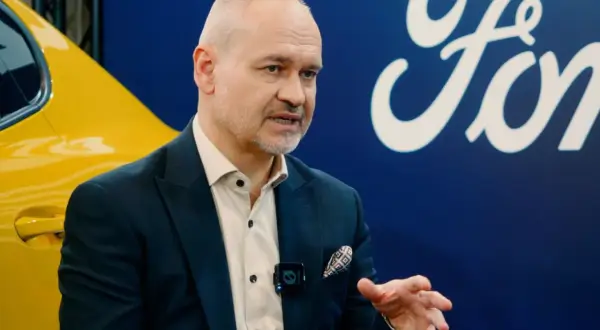 Mężczyzna w garniturze, prawdopodobnie właściciel Forda, rozmawia na tle logo marki i żółtego samochodu.