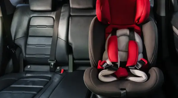 Czerwony fotelik dziecięcy z pasami bezpieczeństwa zamontowany w aucie. System isofix w aucie zapewnia bezpieczne podróżowanie najmłodszych.