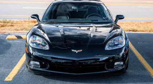 Błyszczący, czarny Chevrolet Corvette, ikoniczna amerykańska marka samochodów, zaparkowany na tle żółtych linii.