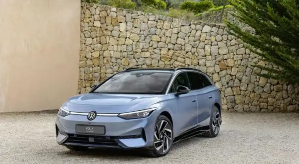 Niebieski Volkswagen ID.7, następca Passata, zaparkowany przed kamiennym murem.