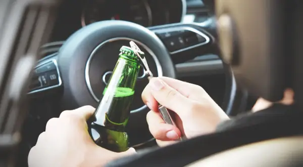 Ręce otwierają butelkę piwa za kierownicą. Nowe kary za jazdę po alkoholu powinny odstraszyć od takiego zachowania.