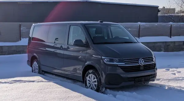 Szare auto 9 osobowe w zimowej scenerii, zaparkowane na śniegu.