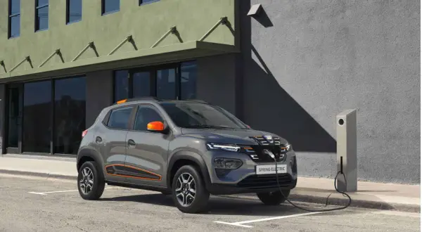 Szary Dacia Spring Electric, z pomarańczowymi akcentami, podłączony do ładowarki. Idealne wymiary do miasta.