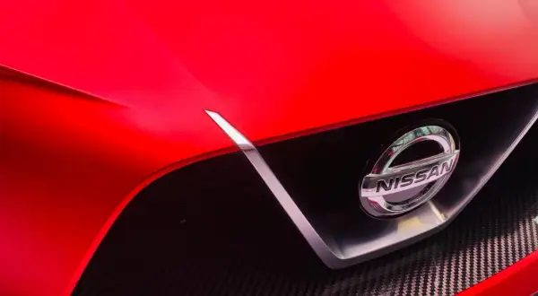 Czerwony Nissan z błyszczącym logo. To jaka to marka? Widać fragment maski i grill z włókna węglowego.