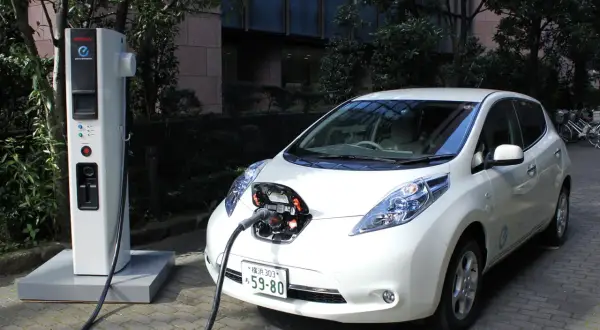 Biały Nissan Leaf podłączony do ładowarki. To przyszłość, czyli serwis samochodów elektrycznych.