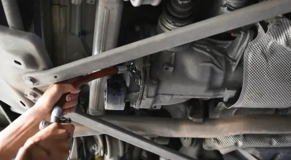 Wymiana oleju w tylnym moście. Mechanik używa wężyka do uzupełnienia płynu.