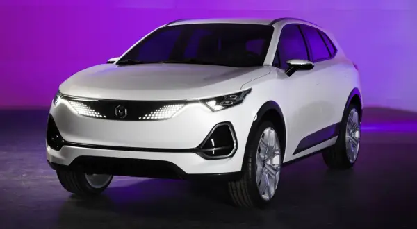Białe, nowoczesne polskie auto elektryczne z futurystycznymi światłami LED, prezentowane na tle fioletowej ściany.