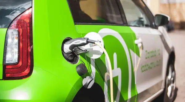Zielony samochód elektryczny podłączony do ładowania. Sprawdź aktualne ceny ładowania samochodów elektrycznych.