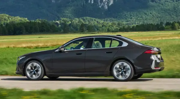 Ciemny sedan BMW jedzie przez malowniczy krajobraz. Idealny do biznesu, gdy rozważasz odliczenie VAT od leasingu samochodu osobowego powyżej 150 tys.