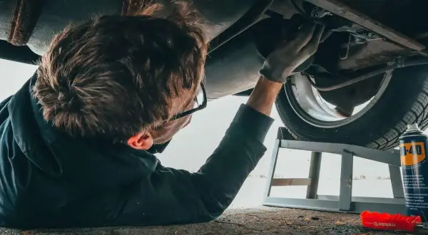 Mechanik podnosi auto sciaga na prawa strone, by naprawić podwozie. W tle puszka WD-40.