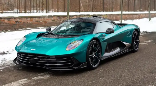 Turkusowy Aston Martin, prawdopodobnie najdroższe auto w Polsce, na tle zimowego krajobrazu z ceglanym murem i płotem.