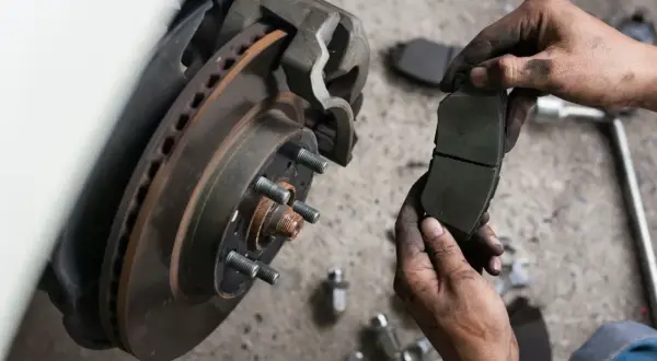 Mechanik pokazuje nowe klocki hamulcowe do wymiany tarcz hamulcowych. Brudne ręce i narzędzia sugerują ciężką pracę.