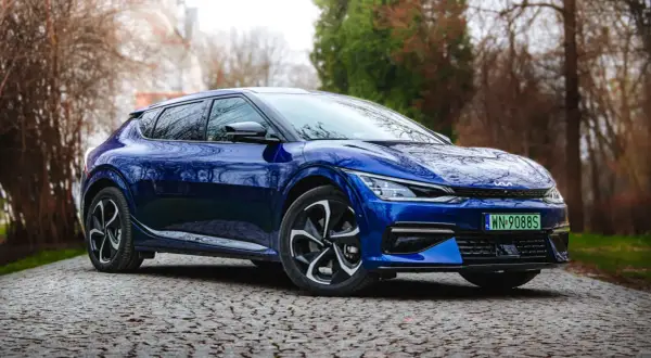 Niebieska Kia EV6 na testowej drodze, wśród drzew. Elegancki design i nowoczesne linie podkreślają jej elektryczny charakter.