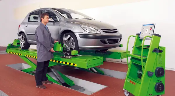 Mechanik sprawdza zbieżność kół samochodu na podnośniku, używając zaawansowanego sprzętu do pomiaru geometrii.