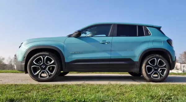 Turkusowy Jeep Avenger, najładniejszy suv, prezentuje się stylowo na tle błękitnego nieba i zielonej trawy.