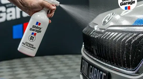 Ręka rozpyla preparat Shiny Garage Citrus Pre Cleaner na grill samochodu, rozpoczynając jego mycie.