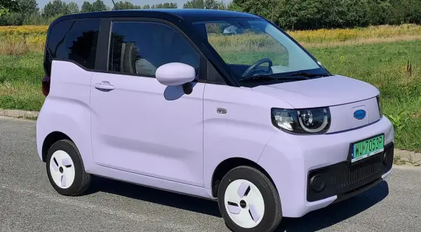 Fioletowy samochód elektryczny na tle łąki. Czy wady samochodów elektrycznych są widoczne w jego kompaktowej budowie?