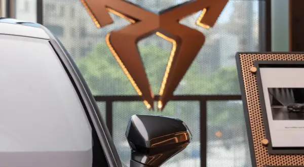 Biały samochód i logo producenta Cupra. Obok zdjęcie nowego modelu Cupra Leon PHEV.