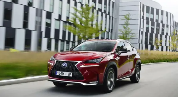 Czerwony Lexus NX, uznawany za najbardziej ekonomiczny SUV, jedzie przed nowoczesnym budynkiem.