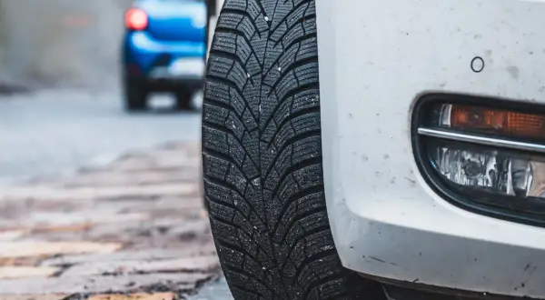 Białe auto z oponami zimowymi na mokrej nawierzchni. Niebezpieczna jazda na letnich oponach w zimie to ryzyko.